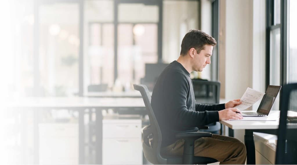 Biller reading a denied explanation of benefits beside a laptop in a bright office